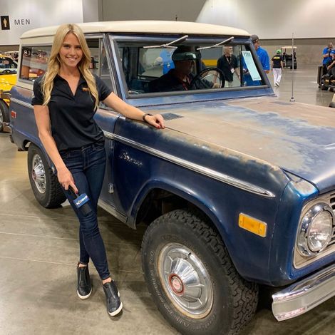 Katie Osborne posing for a picture with a vintage vehicle