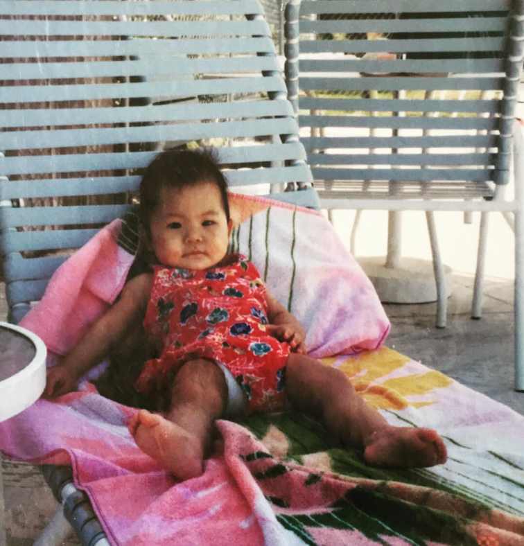 Childhood photo of Nicole Kang laying on the chair.