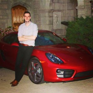 Cooper posing in front of his red Porsche.